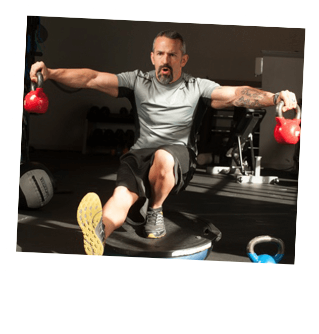 S2 Method Steward Breeding squatting on one leg with two kettle bells in hand